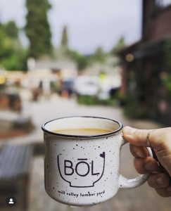 White mug with purple writing spelling BOL with brown liquid inside