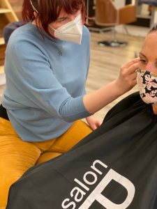 White woman sitting in a barber's chair receiving ear seeds