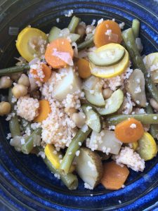 Royal blue bowl filled with zucchini, yellow squash, green beans, carrots, and garbanzo beans over couscous