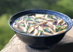 Blue bowl filled with brown broth, mushrooms and green onions