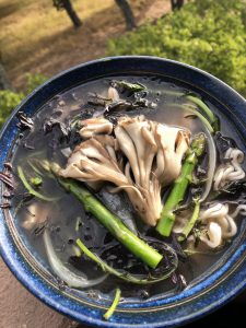Blue bowl filled with broth, black rice ramen noodles, maitake mushroom and asparagus