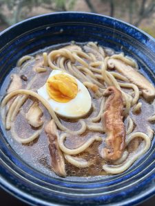 Blue bowl with brown broth, ramen noodles, shitake mushrooms and soft-boiled egg inside